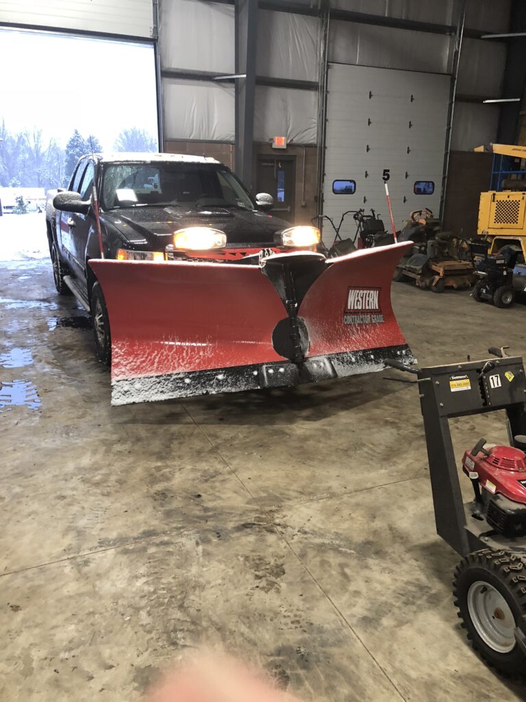 Pickup truck fitted with a red snow plow in the equipment garage