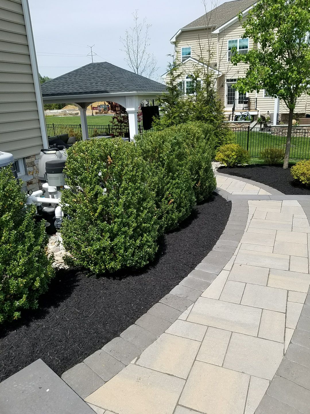 Curved paver walkway lined with fresh black mulch and rounded shrubs